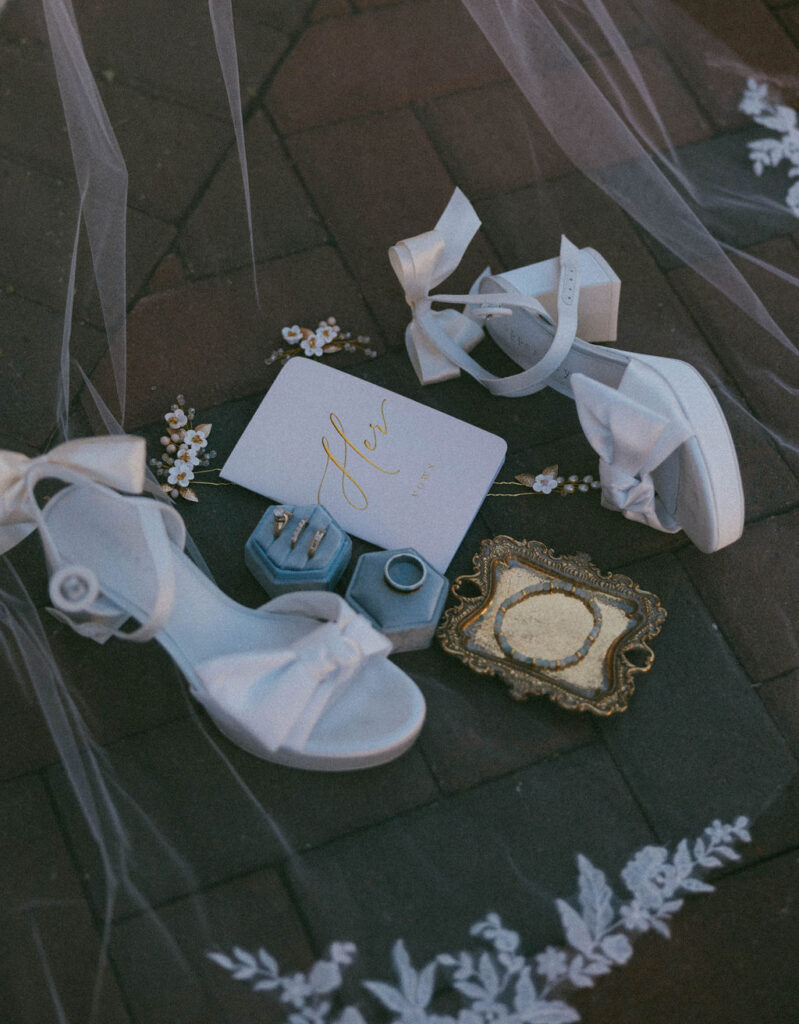 Wedding veil with white heels, her vow book, wedding rings and jewelry flat lay wedding detail photo