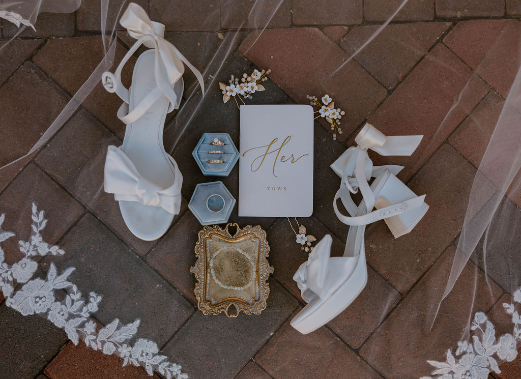 Wedding veil with white heels, her vow book, wedding rings and jewelry flat lay wedding detail photo